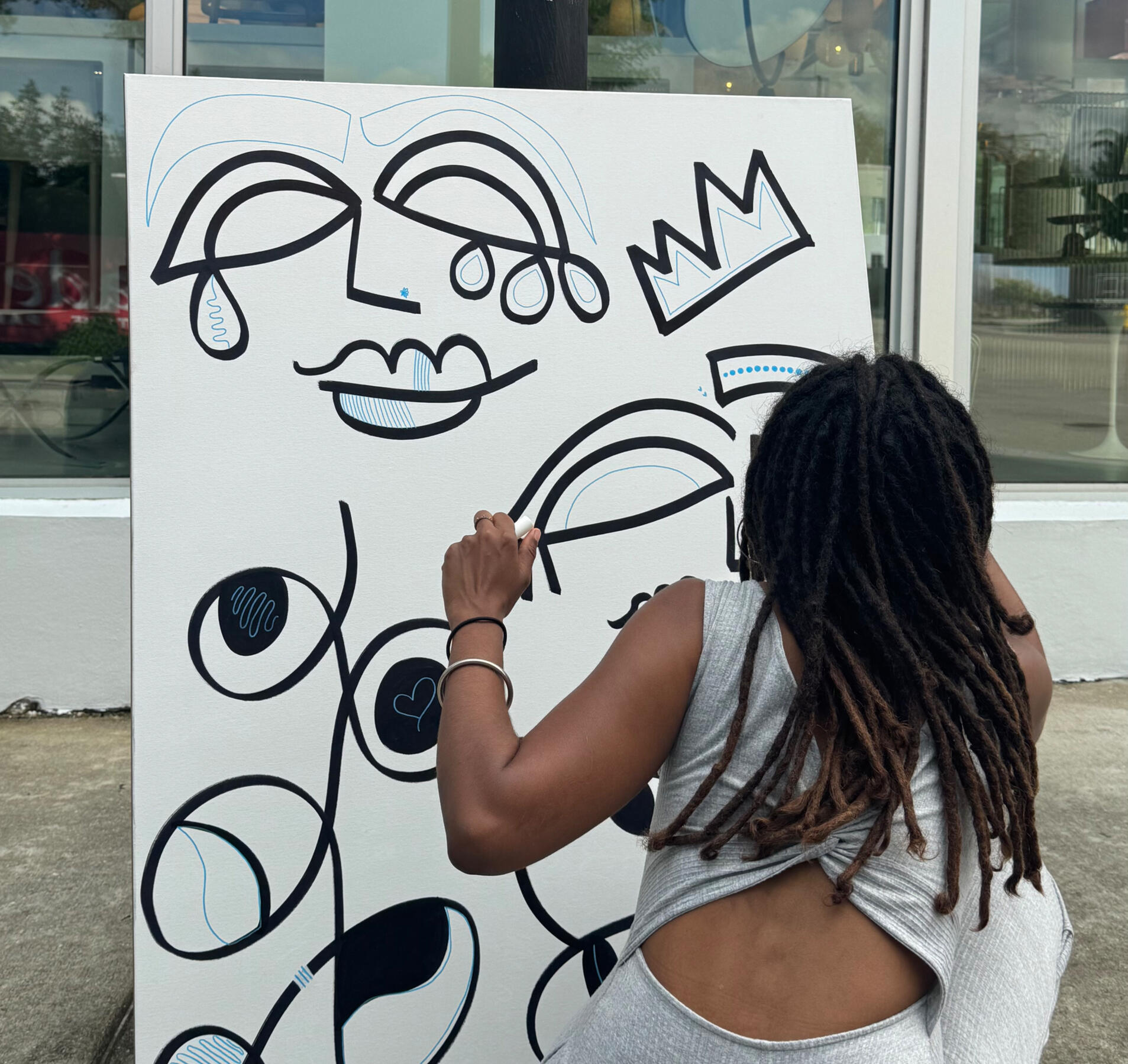 Artist shanelle julia rosita drawing Watch The Throne, a large-scale black marker artwork featuring abstract faces and a crown, outdoors in Miami during 2025 Art Week.