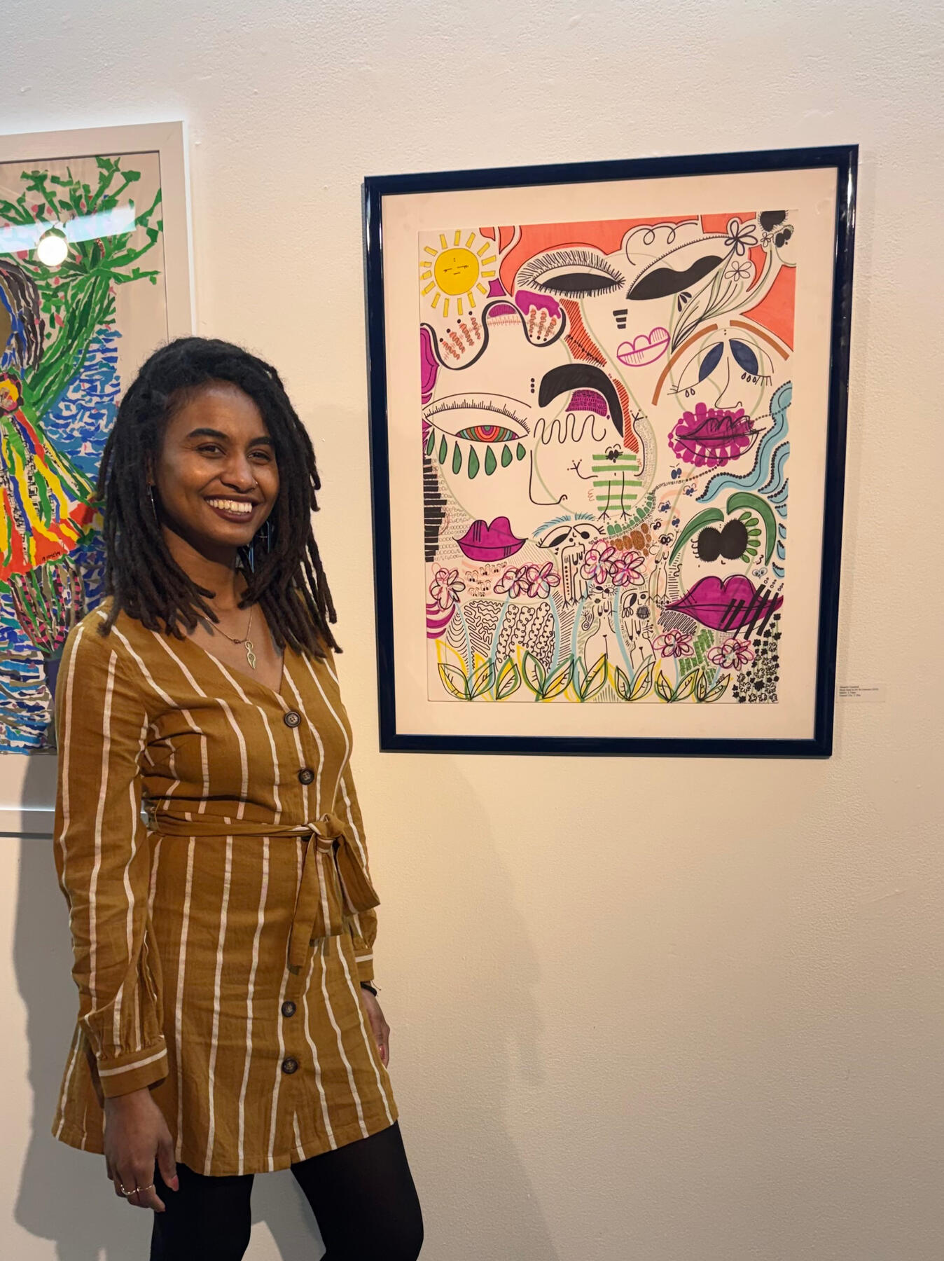 Artist shanelle julia rosita standing beside her framed 2024 marker-on-paper artwork, Black Sand In My St-Germain, during its 2026 exhibition.